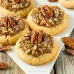 Pecan pie thumbprint cookies, a festive and easy holiday treat, are pictured showcasing their buttery cookie base and gooey pecan filling.