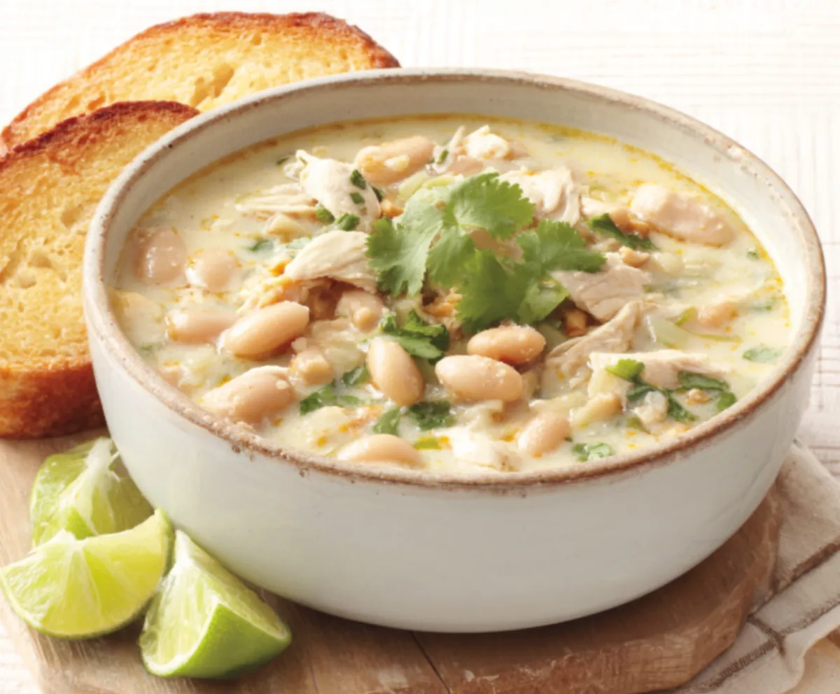 Creamy White Chicken Chili Recipe Close-up shot of creamy White Chicken Chili in a white bowl, garnished with cilantro and a lime wedge.
