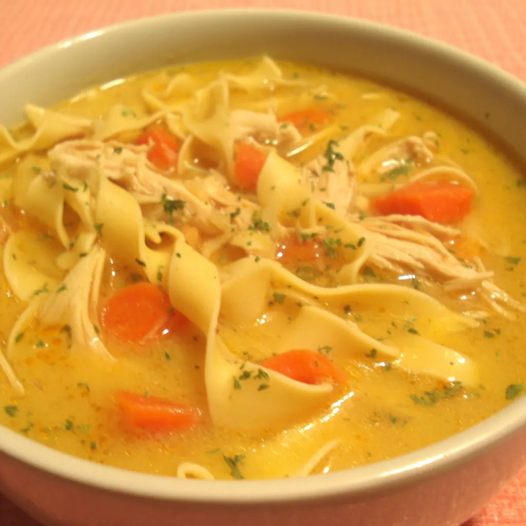 Ginger Garlic Chicken Noodle Soup Close-up of a steaming bowl of Ginger Garlic Chicken Noodle Soup, showcasing the broth, noodles, chicken, and colorful vegetables.