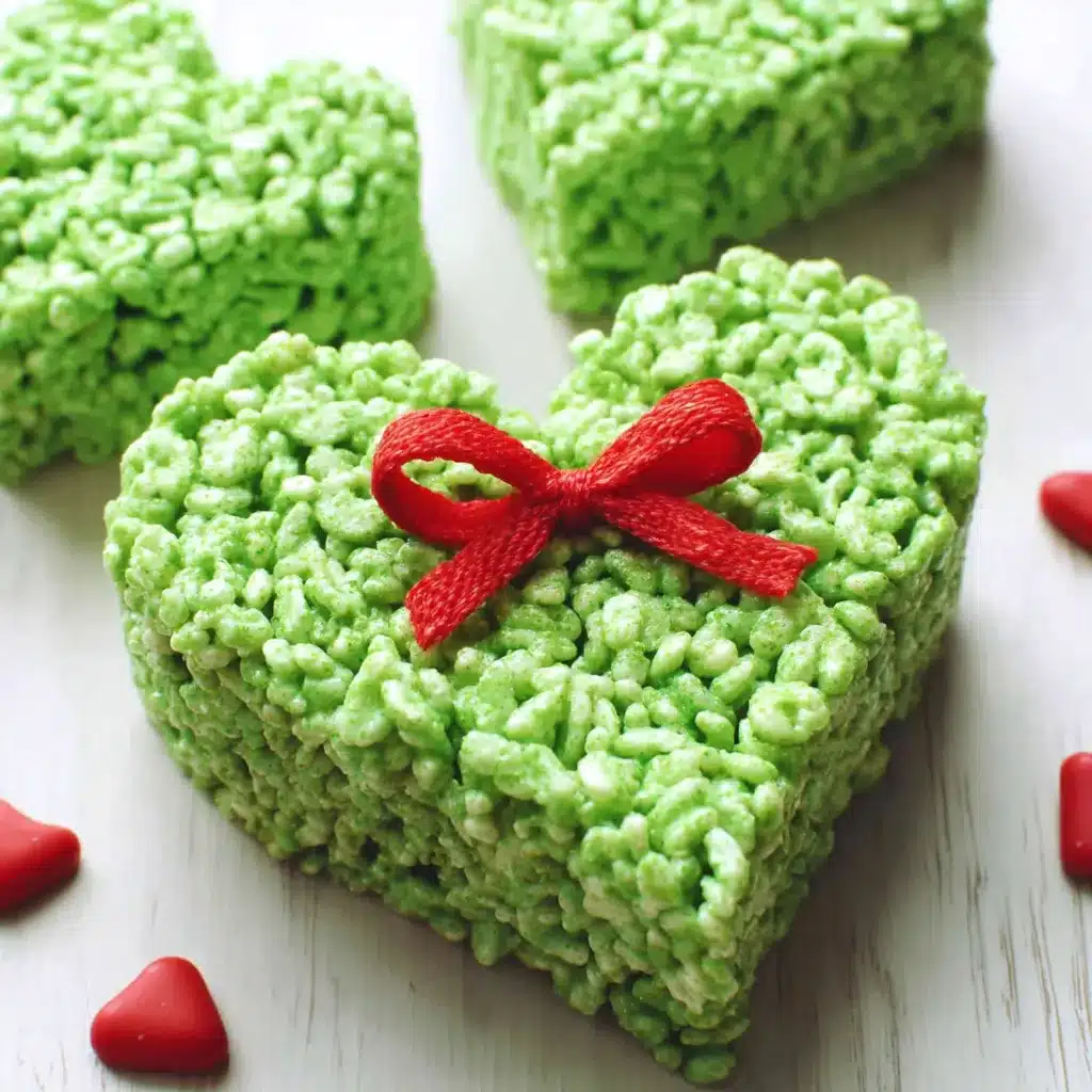 Grinch Heart Krispies Treats Recipe Close-up of homemade Grinch Heart Rice Krispies Treats, showing the green, heart-shaped treats decorated with a red candy heart.