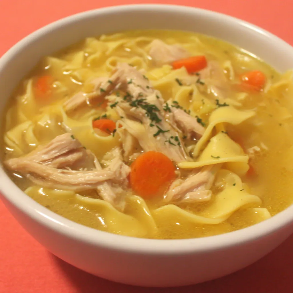 Close-up shot of comforting Ginger Garlic Chicken Noodle Soup in a bowl, showcasing tender chicken, vibrant vegetables, and rich broth.